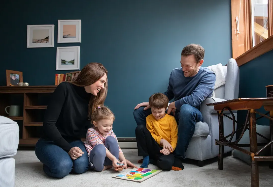 Two adults and two children sitting in a room playing a game on the floor.